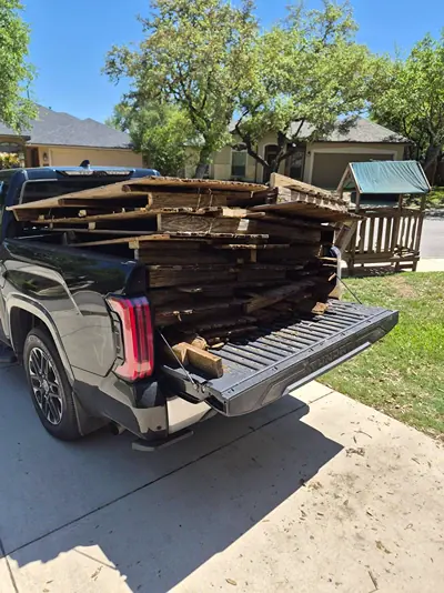 Stacked old lumber and wood boards loaded in the bed of a black pickup truck parked in a driveway