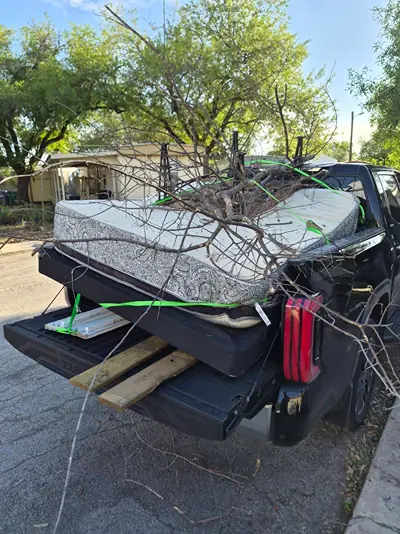 A mattress and tree limbs strapped down with green ratchet straps in the bed of a black pickup truck