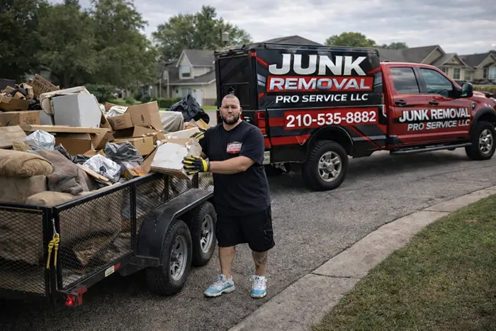 The owner of Junk Removal Pro Service LLC standing beside a trailer loaded with cardboard boxes and household junk, with the company's red service truck parked behind