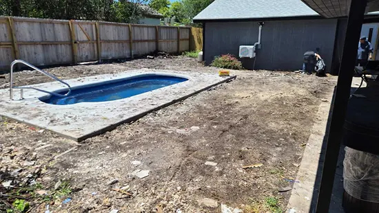 The same backyard after cleanup, with the debris cleared away and only bare dirt around the swimming pool