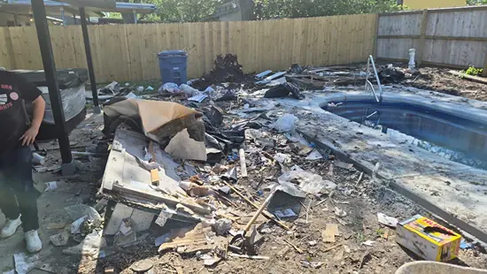 A backyard beside a swimming pool covered in broken wood, insulation, cardboard, and other debris before cleanup