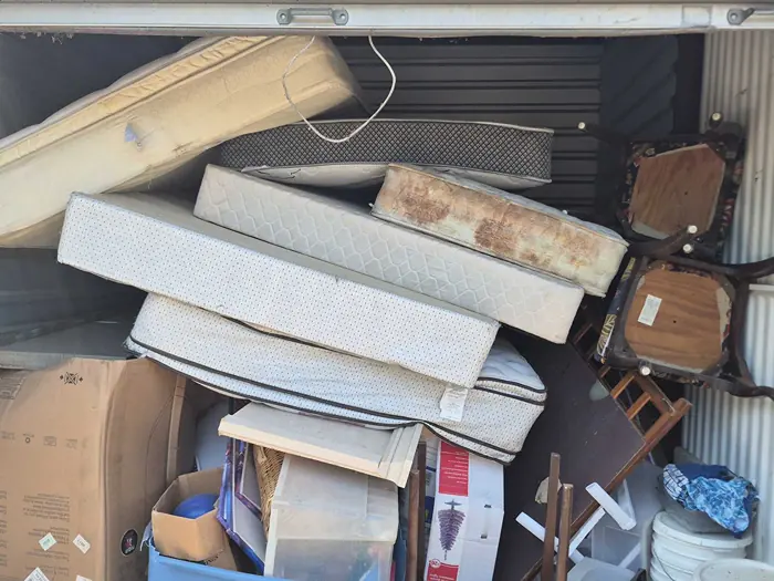 Storage unit packed with old mattresses, chairs, boxes, and furniture before the cleanout